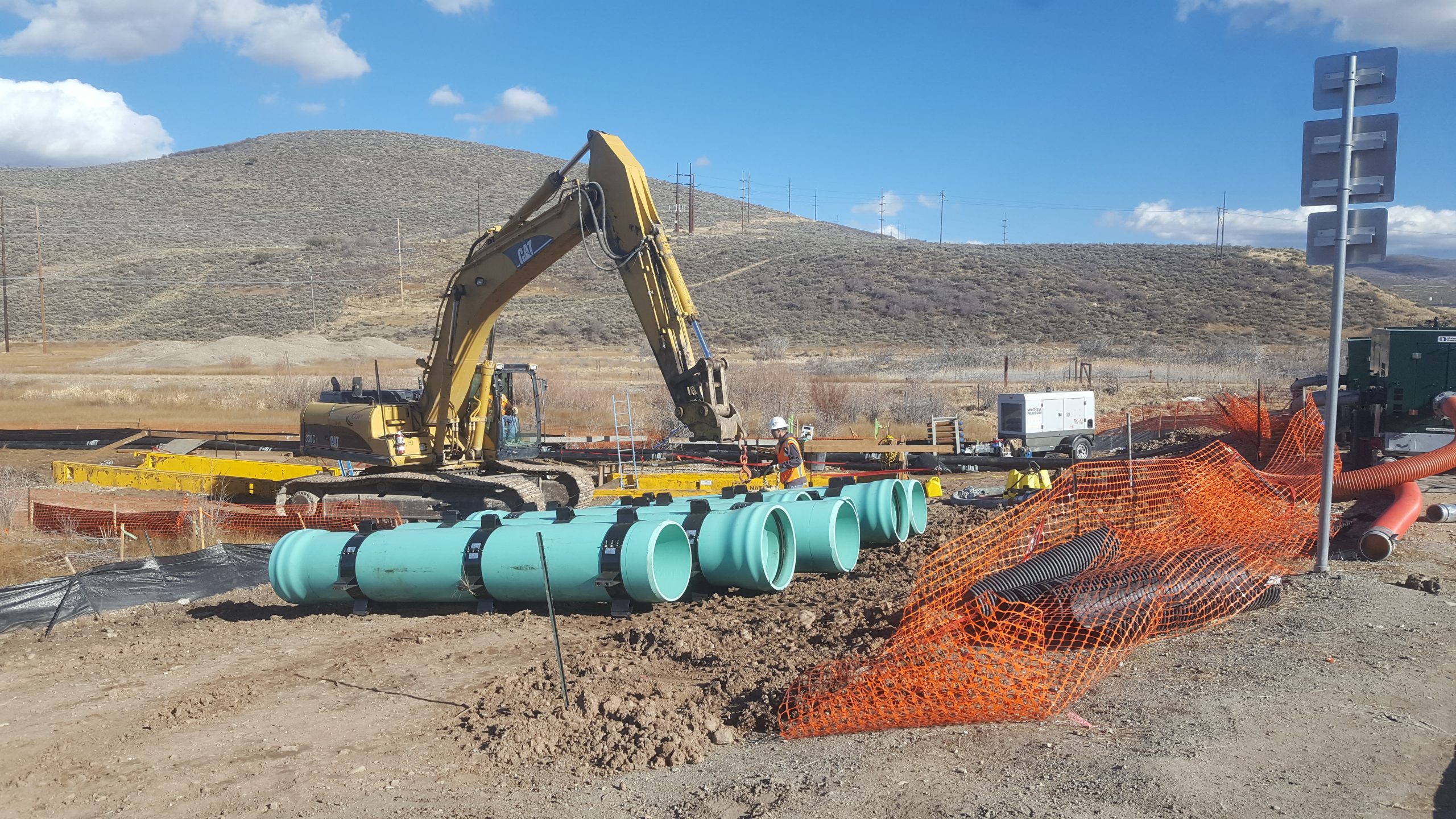 Construction workers and excavator on site of Silver Creek Trunkline Sewer Rehabilitation project standing near large blue pipes.