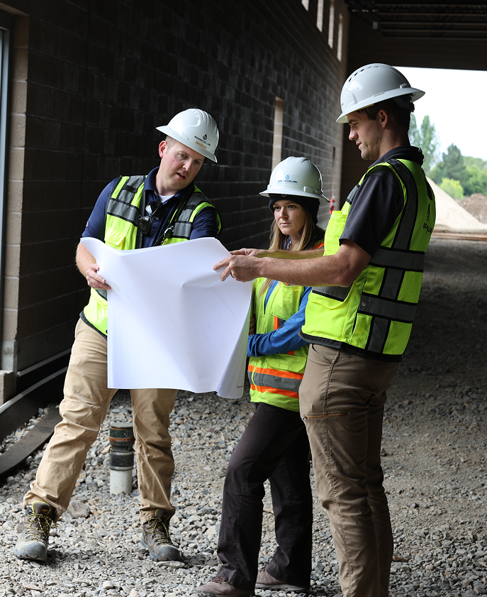 Men and women standing outside in construction hard hats reviewing documents