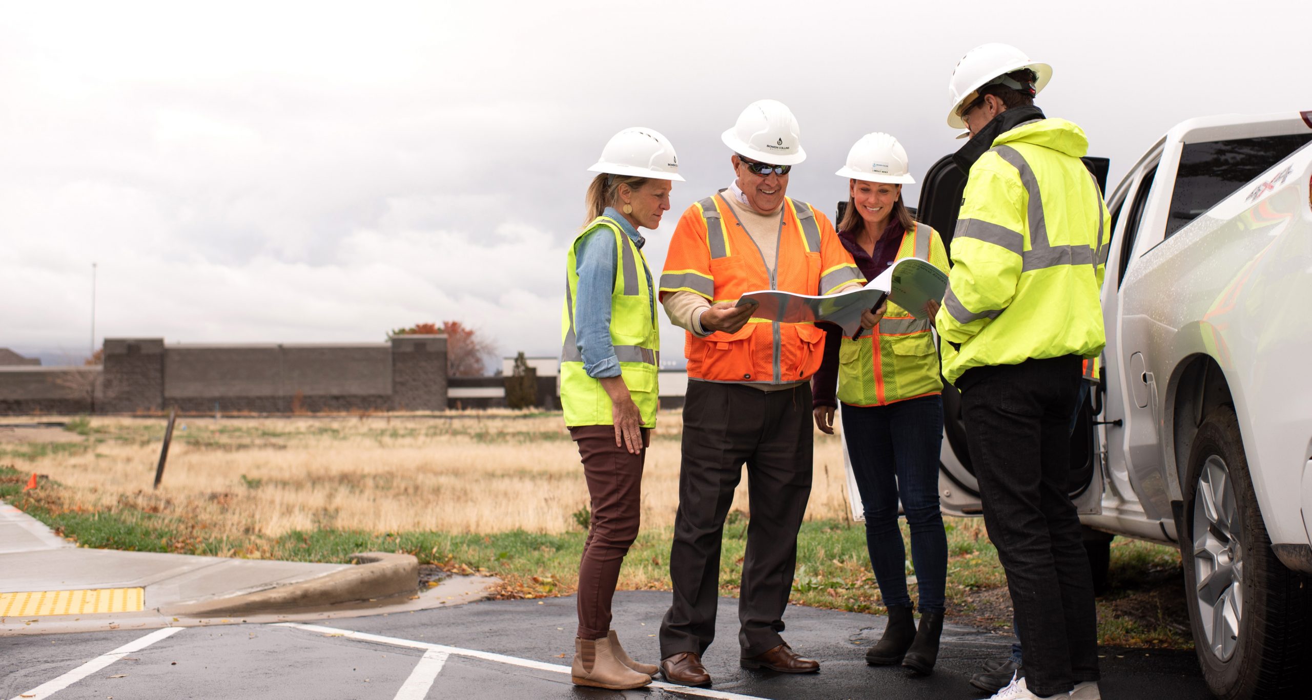 Men and women standing outside in construction hard hats reviewing documents